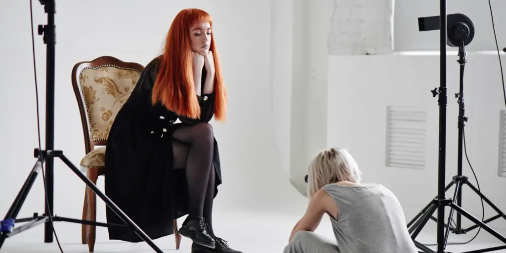 Rothaarige Frau posiert im Studio-Sessel, Fotografin macht Foto vom Boden